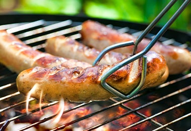Las salchichas y las pinzas no pueden faltar en un asado. Salchichas a la parrilla, con pinzas para darles vuelta.