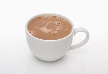 Taza de chocolate caliente espeso servida en taza blanca sobre fondo claro.