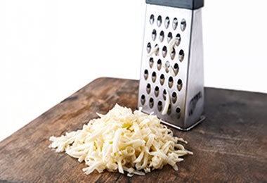 Queso blanco rallado junto a rallador sobre tabla de cocina.