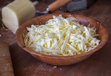 Queso blanco rallado en tazón de madera, listo para acompañar bebidas calientes.
