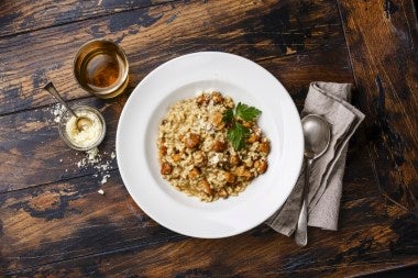 Arroz tipo arborio en plato de risotto italiano, junto con cuchara, bebida y un dip.