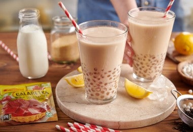 Dos vasos con bebida de perlas de tapioca, juntos a tarros de leche, limones y azúcar.