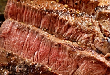 Tiras de carne asada en rodajas con especias sobre tabla de madera.