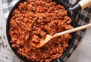 Sartén llena de carne molida, o picada, siendo revuelta con un cucharón de madera.