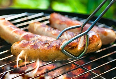 Varios chorizos sobre una parrilla de carbón y con unas pinzas