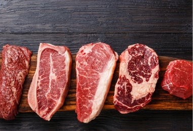 Selección de cortes crudos de carne roja sobre fondo oscuro.