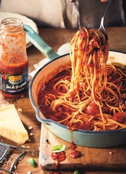 Espagueti servido con salsa putanesca, acompañado de queso parmesano y albahaca