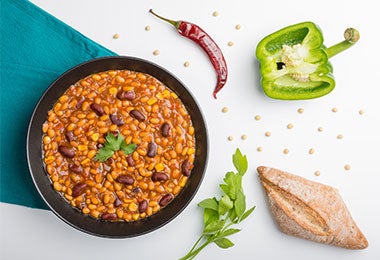 Chili con carne servido con pimientos verdes, maíz y pan rústico.