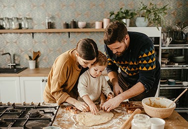 Pareja de padres preparando masa para galletas junto a su pequeño hijo.