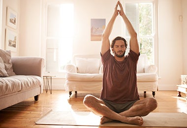 Hombre estirando para empezar a practicar yoga en casa con los ojos cerrados