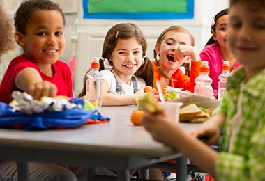 Grupo de niños disfrutando de su comida en el colegio, mostrando ideas de loncheras prácticas y equilibradas.