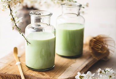 Matcha latté acompañado de unas flores blancas sobre una tabla, una de las bebidas calientes con leche más tradicionales que puedes preparar