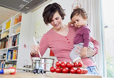 Mujer cocinando con una olla de acero inoxidable junto a su hija.