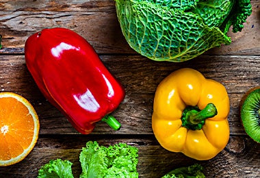 Un pimentón rojo y uno amarillo, acompañados de otras frutas y verduras.