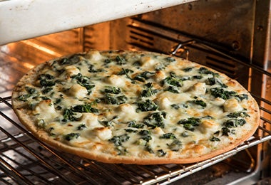 Pizza con queso, pollo y hojas verdes en un horno para celebrar su Día Mundial