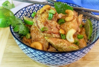 Bowl con pollo en salsa de marañones, decorado con cebolla fresca, cilantro y marañones enteros, acompañado de limón y palillos