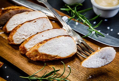 Filetes de pollo sobre tabla de picar de madera para almuerzos balanceados.
