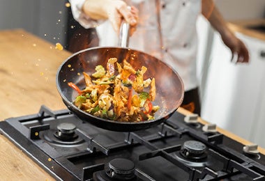 Cocinero salteando vegetales profesionalmente en una sartén.