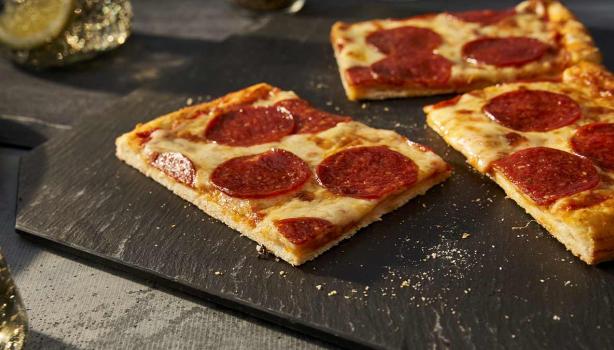 Porción de pizza de pepperoni con una masa delgada sobre un plato negro para celebrar su Día Mundial