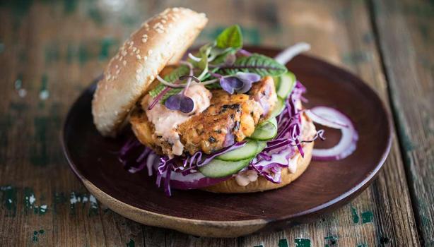 Apetitosa hamburguesa de pescado con vegetales emplatada y sobre una mesa de madera