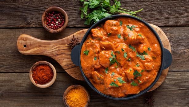 Butter Chicken con cilantro y acompañado de especias sobre tabla de madera