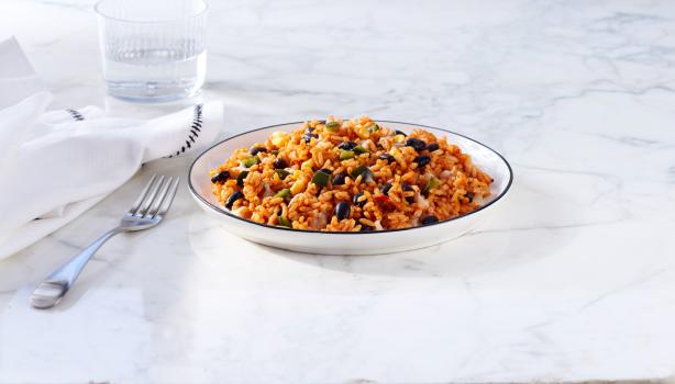 Plato hondo de arroz con habichuela junto a un tenedor, vaso de agua y servilleta.