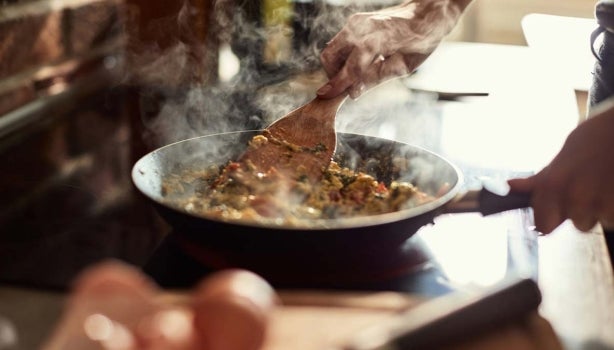 Persona cocinando huevos en un sartén con la guía de cocina para principiantes.