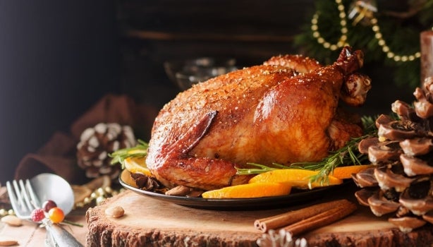 Pollo asado entero en bandeja con tajadas de mango y sobre mesa rústica.