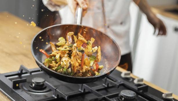 Chef profesional salteando verduras con pollo en una sartén.