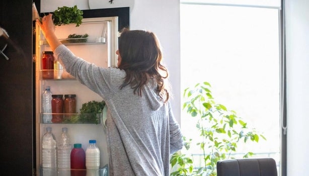 Mujer almacenando idealmente vegetales en su nevera.