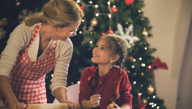 Madre e hija preparando galletas juntas mientras disfrutan el ambiente típico de las películas de Navidad.