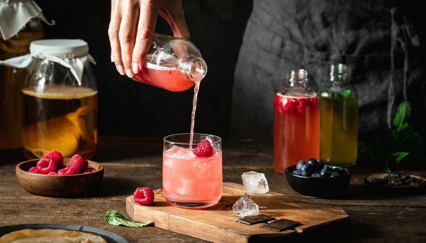 Vaso de kombucha rosada con hielo y frambuesa, servido desde una botella.