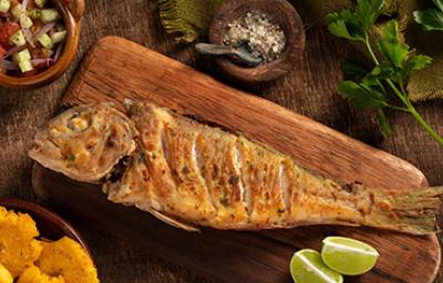 El pescado frito es crujiente y suele servirse con limón. Un pescado frito entero, servido sobre una tabla y acompañado con limón.