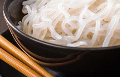 Los noodles de arroz se usan para acompañar diferentes platos. Noodles de arroz, servidos en un plato negro, junto a unos palillos chinos.