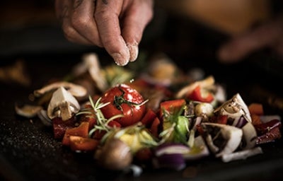 Una persona usando sal para sazonar unas verduras.
