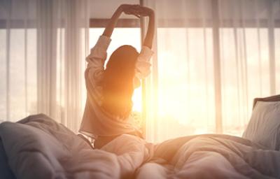 Una mujer con buenos hábitos de sueño estirando en la cama Una mujer con buenos hábitos de sueño estirando en la cama