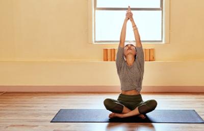 Mujer practicando yoga en casa encima de una esterilla y con los brazos estirados hacia arriba Mujer practicando yoga en casa encima de una esterilla y con los brazos estirados hacia arriba