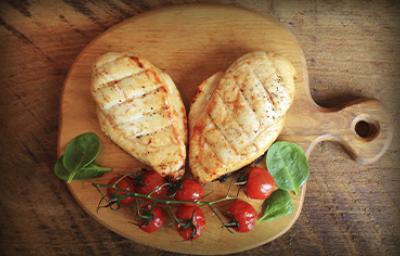 Dos pechugas de pollo con un racimo de tomates cherry, una comida con proteínas magras encima de una tabla Dos pechugas de pollo con un racimo de tomates cherry, una comida con proteínas magras encima de una tabla