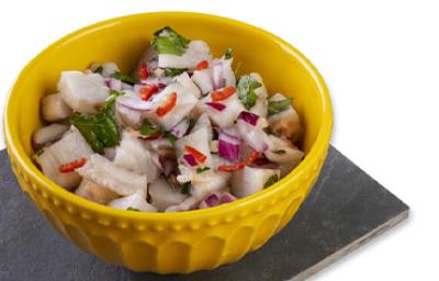 Ceviche con leche de tigre, cebolla morada, cilantro y limón en un recipiente amarillo sobre un fondo blanco Ceviche con leche de tigre, cebolla morada, cilantro y limón en un recipiente amarillo sobre un fondo blanco