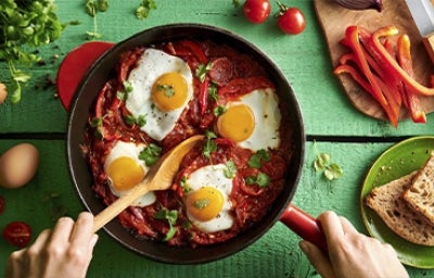 Huevos shakshuka con hierbas, salsa de tomate, pan y pimentón picado en toma cenital Huevos shakshuka con hierbas, salsa de tomate, pan y pimentón picado en toma cenital