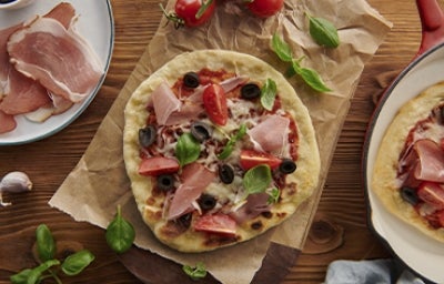 Mesa con pizza de prosciutto con aceitunas, tomates y rúgula Mesa con pizza de prosciutto con aceitunas, tomates y rúgula