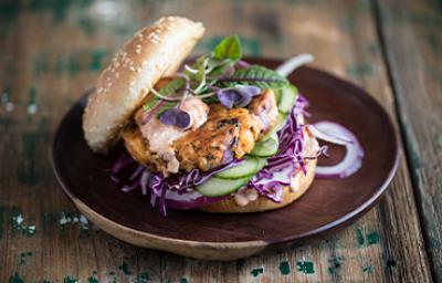 Apetitosa hamburguesa de pescado con vegetales emplatada y sobre una mesa de madera