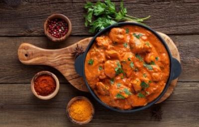 Butter Chicken con cilantro y acompañado de especias sobre tabla de madera
