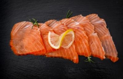 Salmón ahumando en frío, un delicioso manjar. Pequeños trozos de salmón ahumado frío sobre fondo negro.