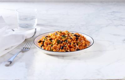 Plato hondo de arroz con habichuela junto a un tenedor, vaso de agua y servilleta.
