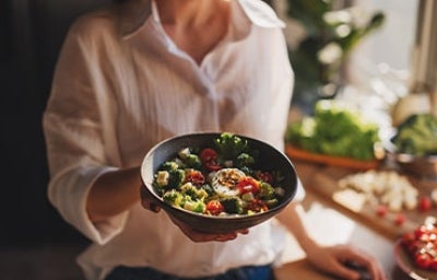Mujer con un plato de ensalada de brócoli con huevo duro y tomate, almuerzo balanceado.