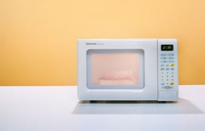 Limpieza del microondas, fundamental para la higiene y el sabor. Microondas siendo utilizado sobre una mesa blanca y con un fondo amarillo.
