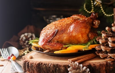 Pollo asado, parte esencial del menú con pollo colombiano. Pollo asado entero en bandeja con tajadas de mango y sobre mesa rústica.