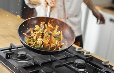 Chef profesional salteando verduras con pollo en una sartén.