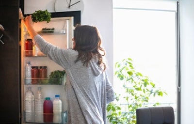 Mujer almacenando idealmente vegetales en su nevera.